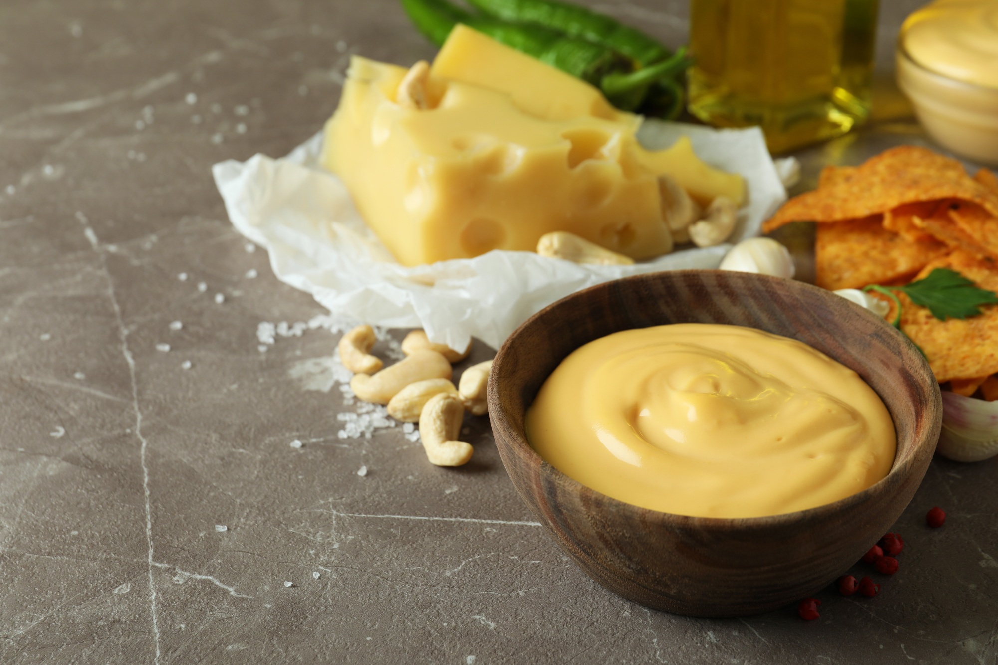 Bowls with cheese sauce and ingredients on gray textured table