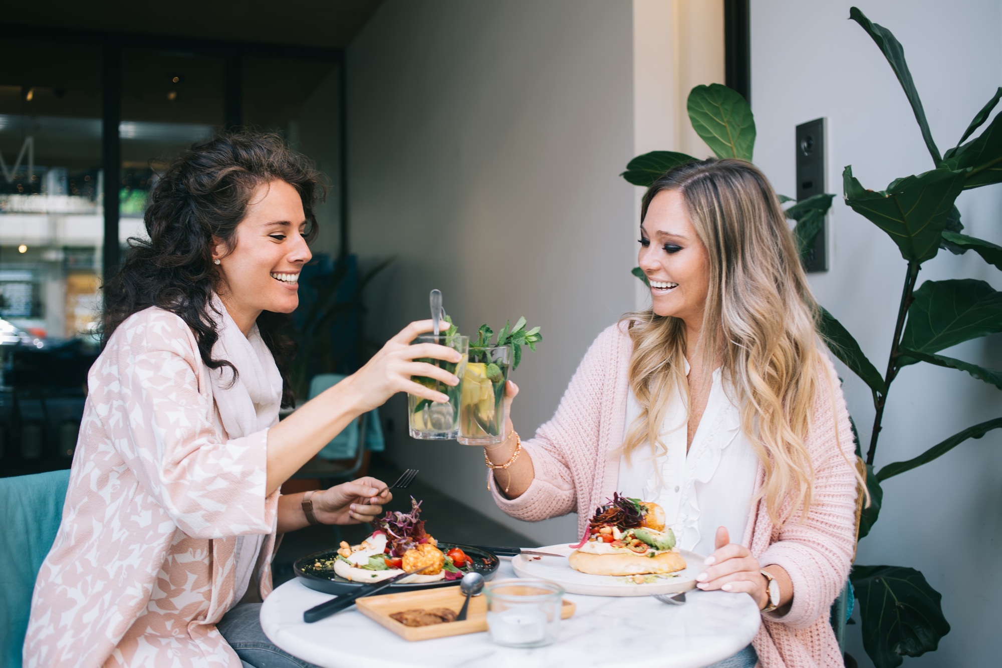 smiling women 20s eating healthy meal and talking to each other on lunch break with beverages