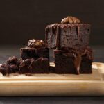 Stack of baked square pieces of chocolate brownie cake on brown wooden cutting board