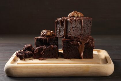 Stack of baked square pieces of chocolate brownie cake on brown wooden cutting board