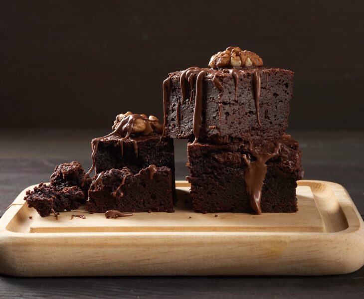 Stack of baked square pieces of chocolate brownie cake on brown wooden cutting board