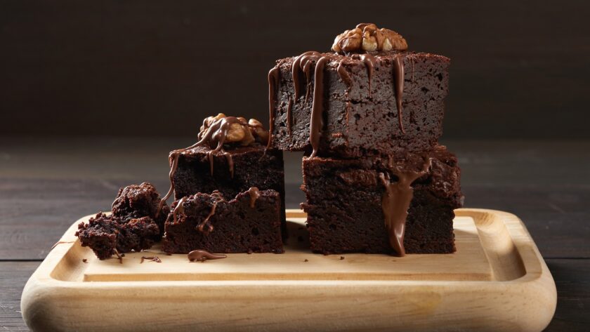 Stack of baked square pieces of chocolate brownie cake on brown wooden cutting board