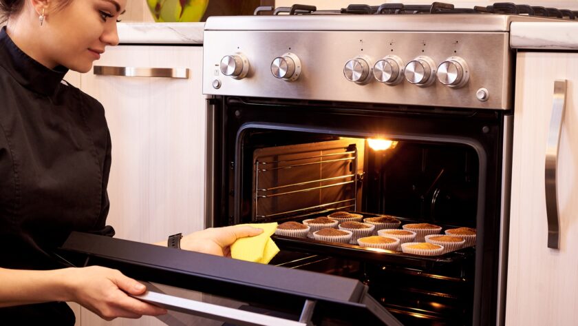 Young woman cooking cupcakes in the oven