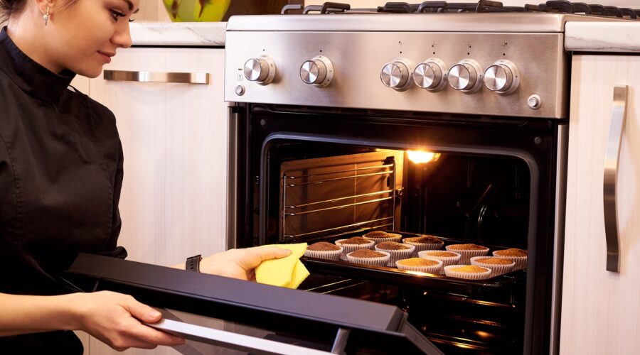 Young woman cooking cupcakes in the oven