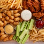 Fried chicken strips and french fries board with sauces and celery