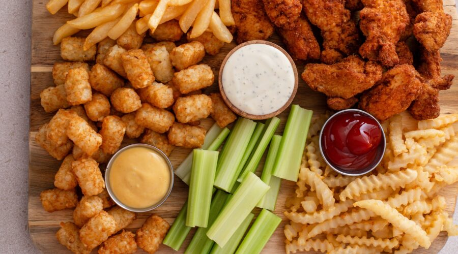 Fried chicken strips and french fries board with sauces and celery