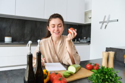 Portrait of beautiful smiling woman, writing her healthy menu, eating tomato while cooking, making
