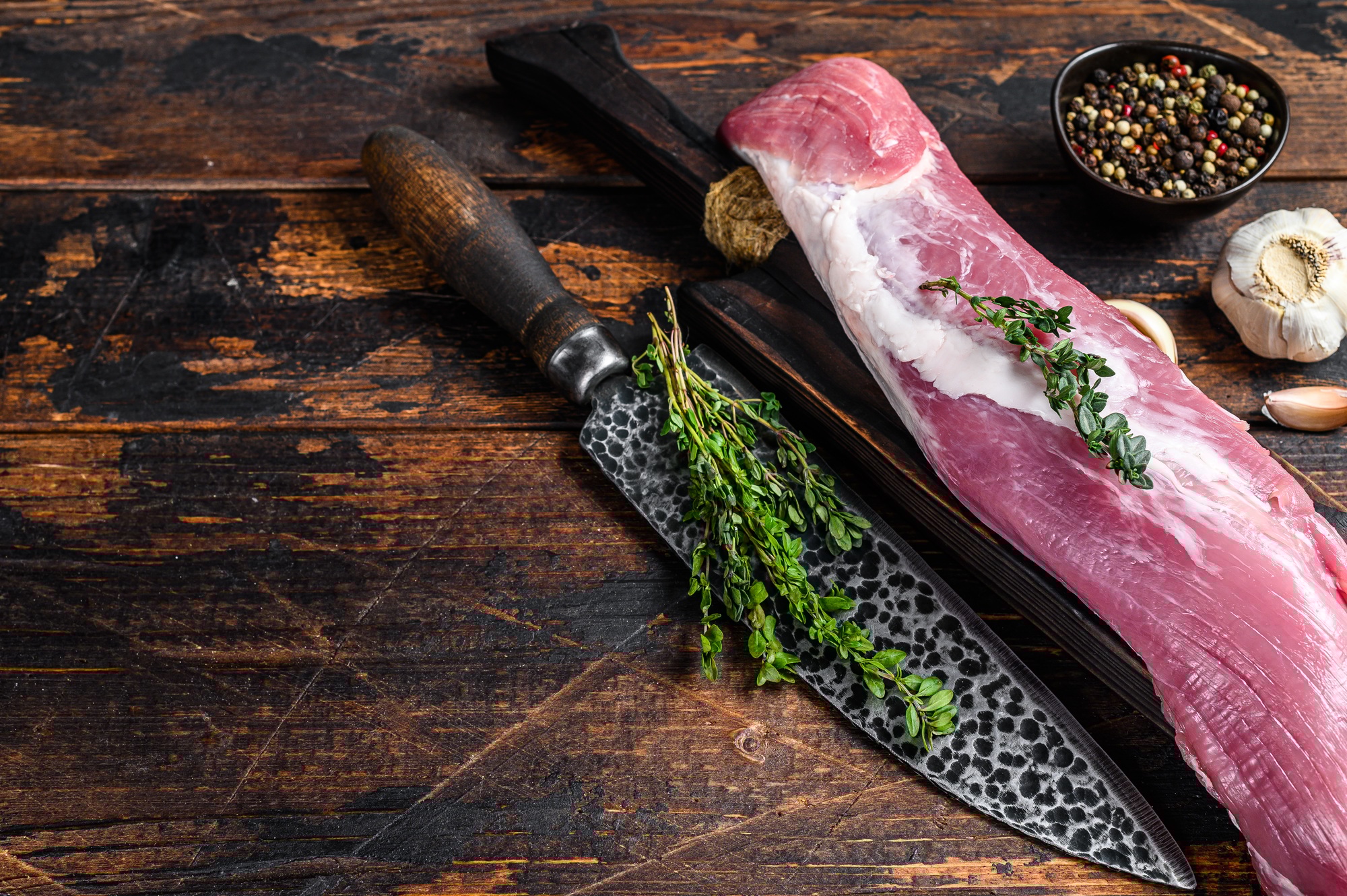 Raw fresh pork tenderloin meat on a cuuting board with cleaver.