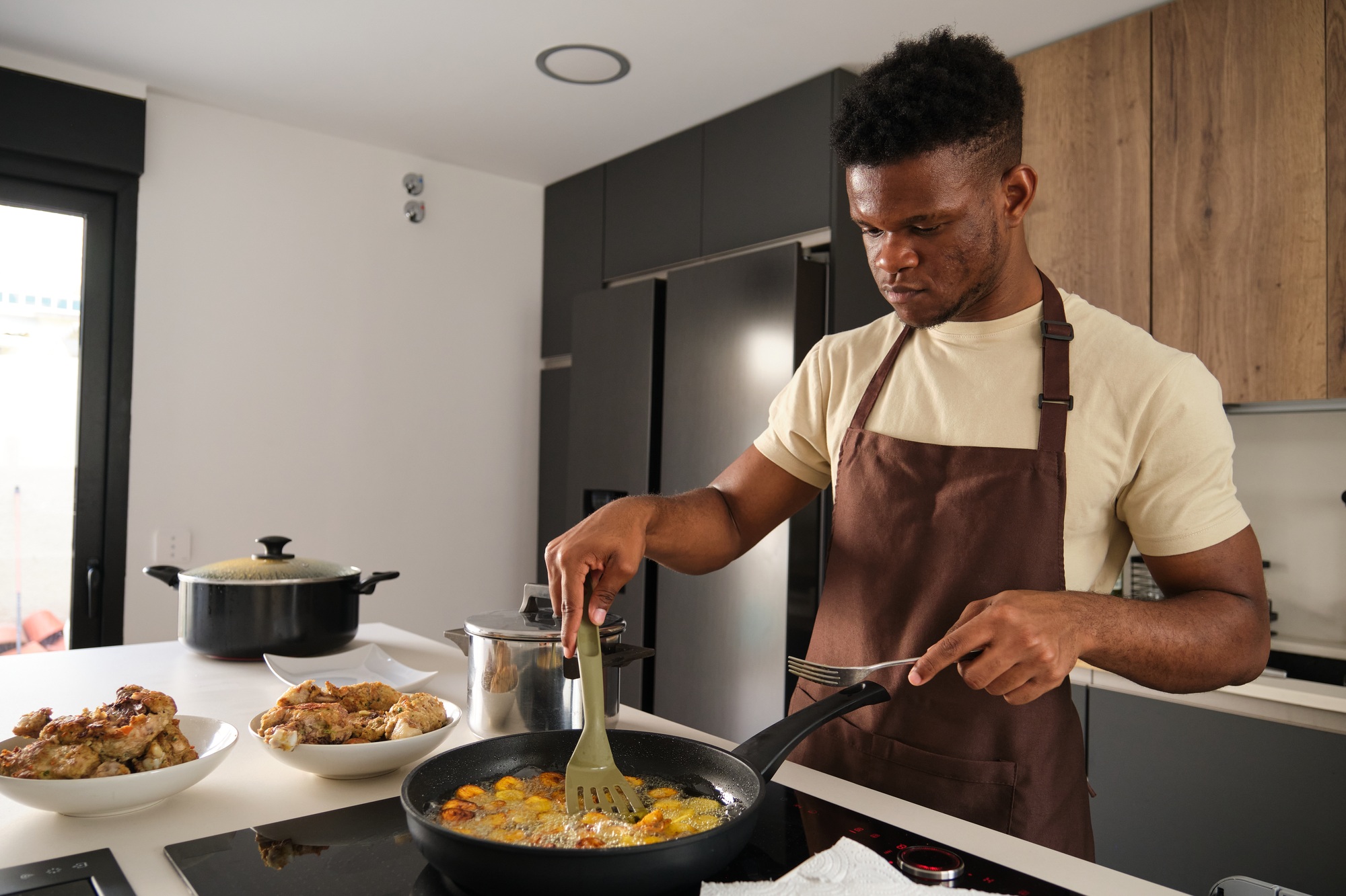 Young black man frying plantains slices.